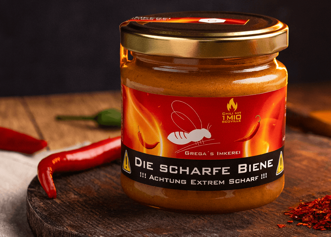 "Nahaufnahme von 'Die Scharfe Biene' Honig neben einer einzelnen Carolina Reaper Chili auf rustikalem Holzuntergrund."
