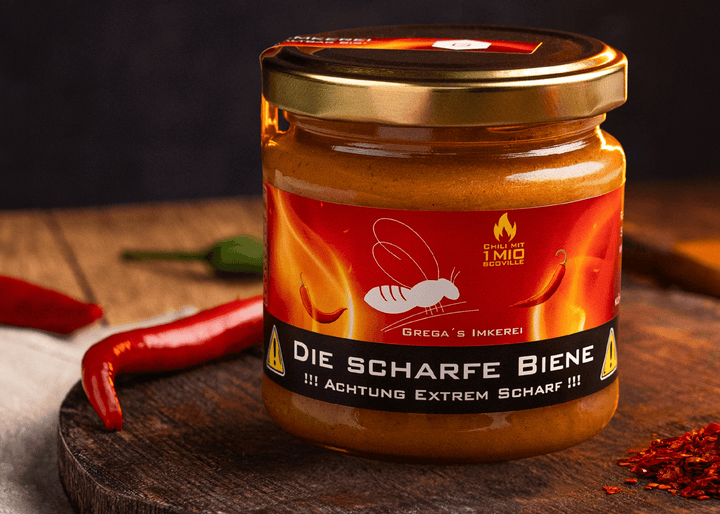 "Nahaufnahme von 'Die Scharfe Biene' Honig neben einer einzelnen Carolina Reaper Chili auf rustikalem Holzuntergrund."