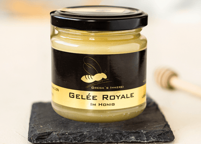 Gelée Royal im Honig 250g Glas steht auf Schieferplatte daneben liegt ein Holzhoniglöffel um mit dem Genießen zu beginnen.