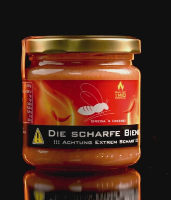 "Geöffnetes Honigglas mit CAROLINA REAPER IM HONIG von 'Die Scharfe Biene', der goldene Honig reflektiert Licht, betont durch die dunkle Chili."